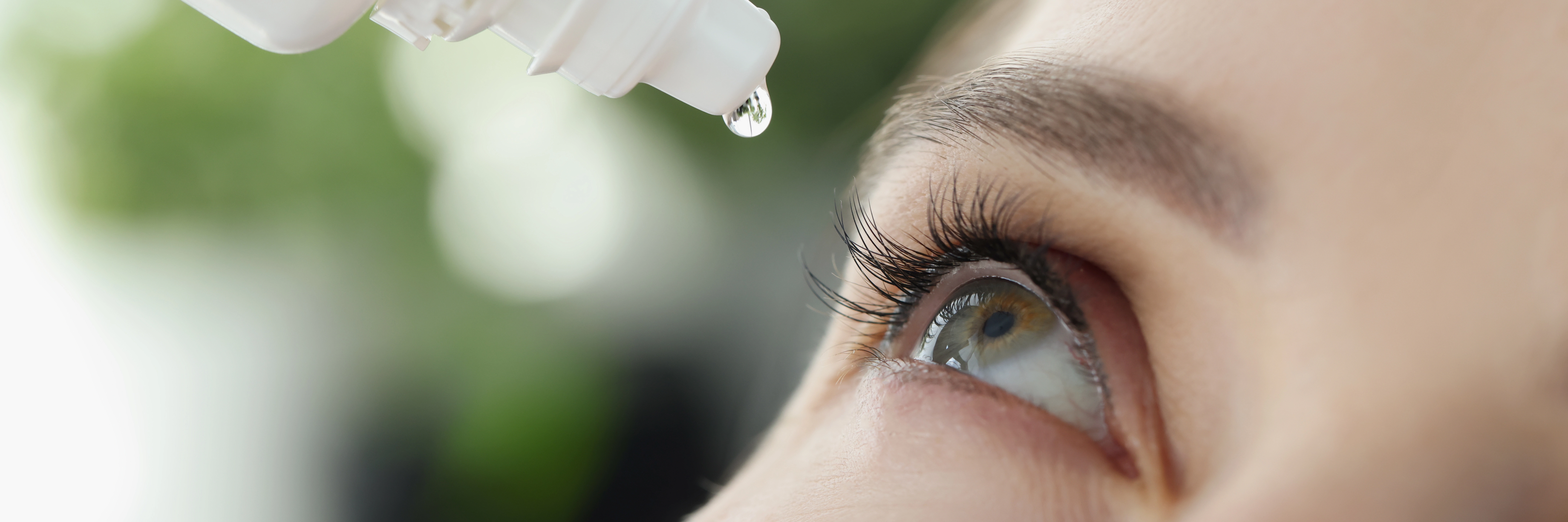 A close up picture of a woman putting eye drops in her eyes.